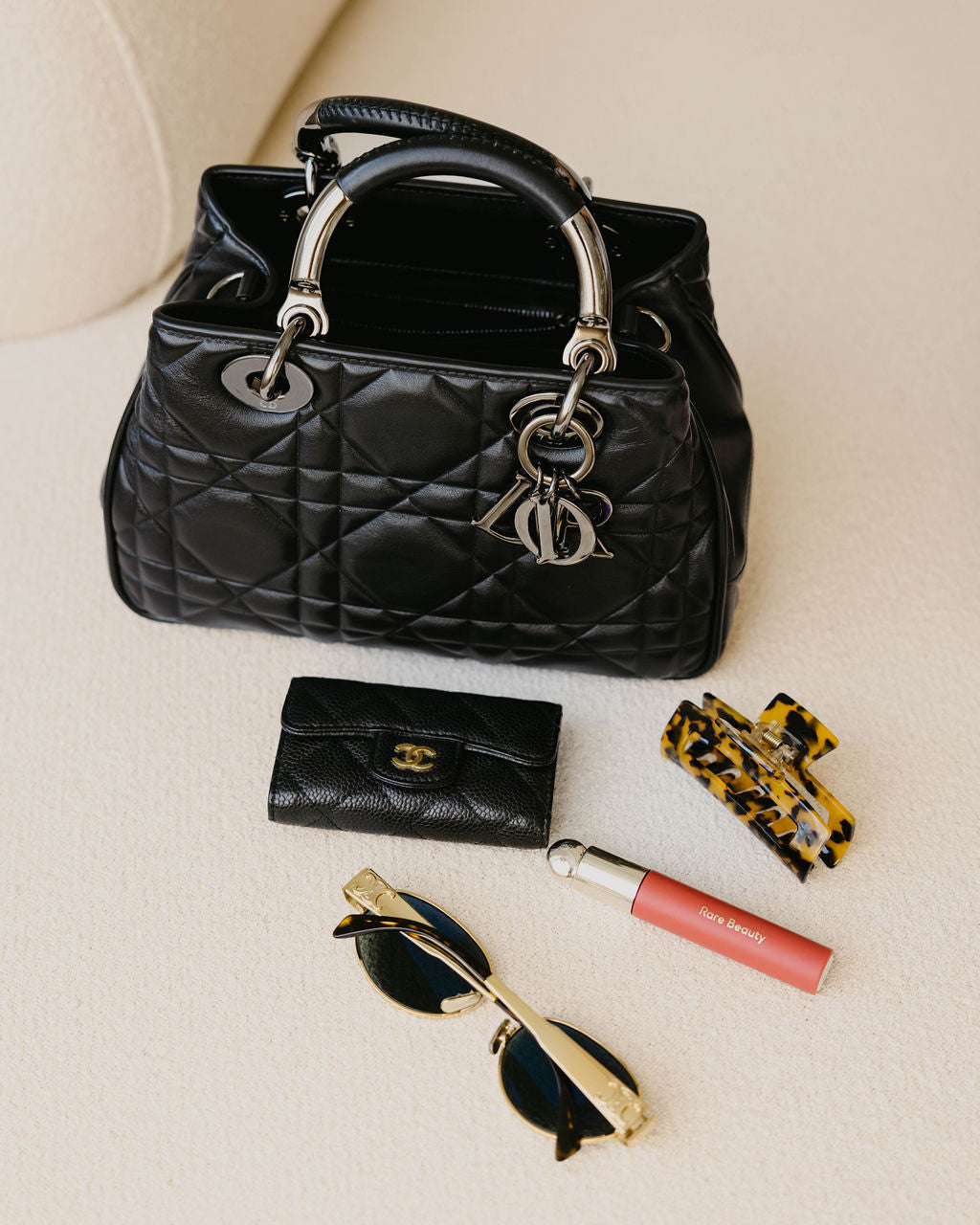 A used luxury handbag by Dior with a used luxury wallet by Chanel on asleek cream colored couch.