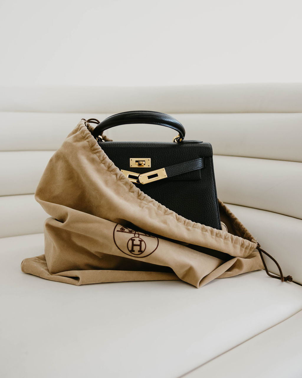 A used luxury handbag by Hermes encased in a velvet bag and sitting on a cream colored couch