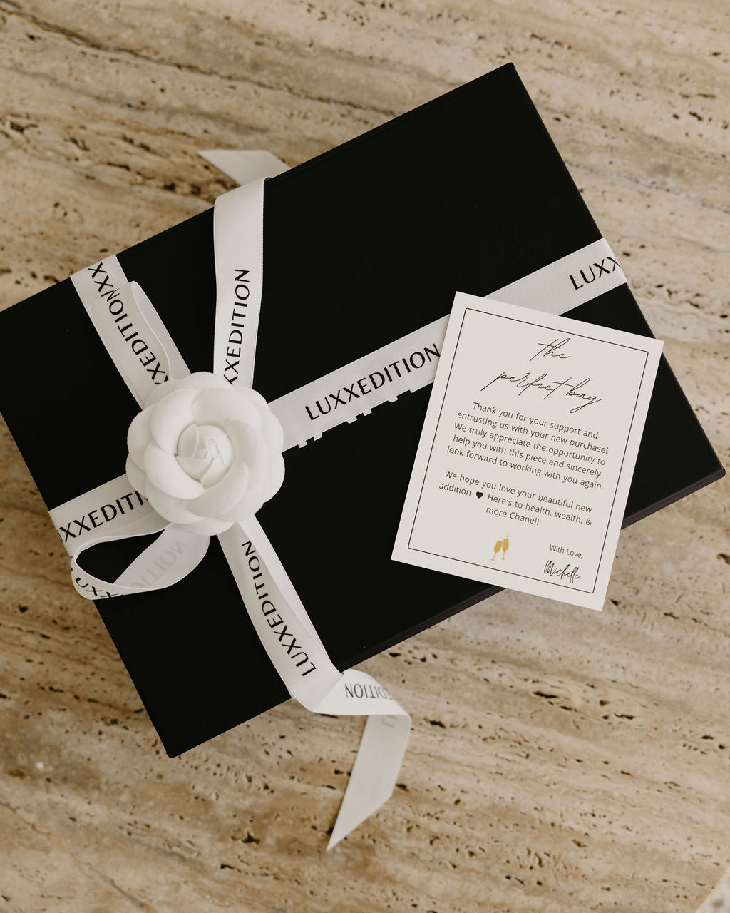 Luxxedition unboxing experience for all buyers of Luxury Bag Consignment & Resale featuring a black box adorned with white ribbon and a hand-written note. 