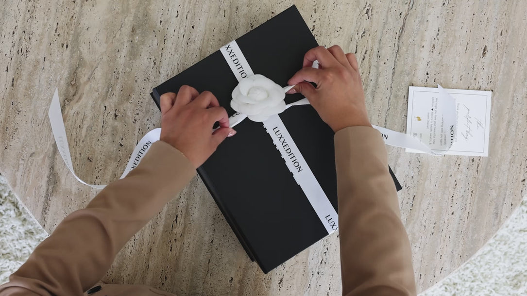 Luxxedition unboxing video showing a luxury black black and white ribbon holding a preloved luxury Chanel handbag